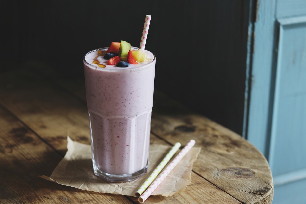 A refreshing Greek yogurt smoothie topped with colorful fruits and served with striped straws.